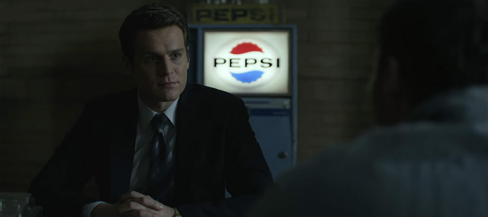 Jonathan Groff as Holden Ford sitting in a dark room, his face illuminated by a giant Pepsi logo on a vending machine behind him