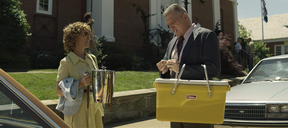 Holt McCallany as Bill Tench lights a cigarette outside while holding a yellow vintage Coleman cooler