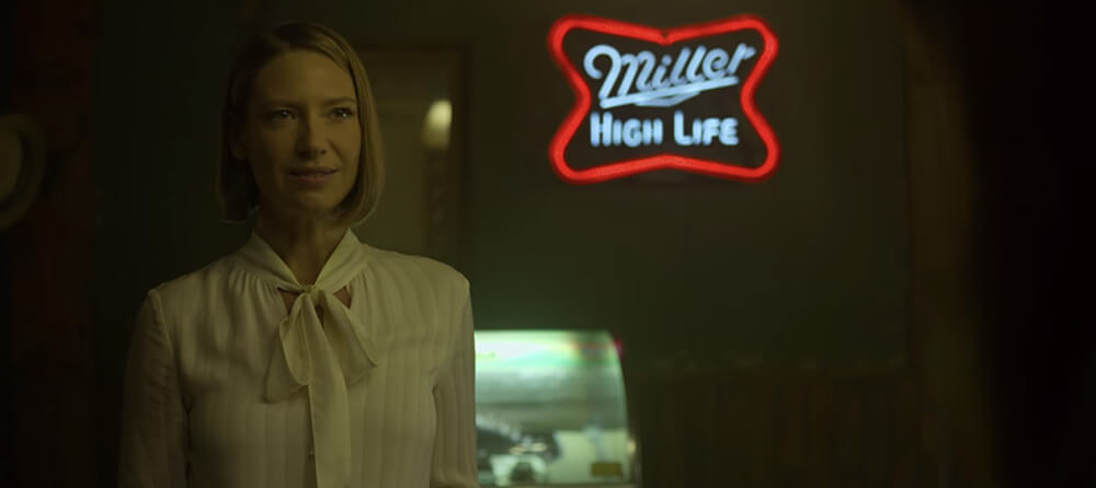 Anna Torv as Wendy Carr in a dark bar with a neon Miller High Life sign behind her, the sign is more centered in the shot than she is