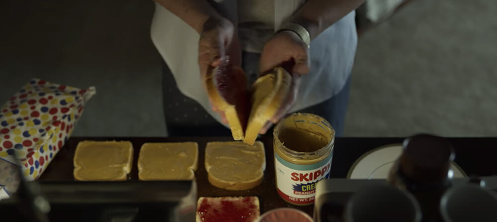 a man is making peanut butter and jelly sandwiches with Skippy and Wonder Bread