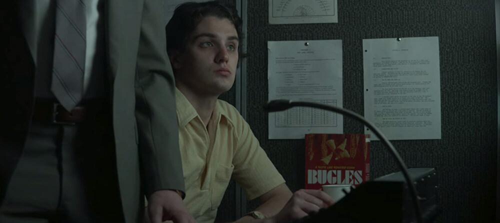 a technician sits in a surveillance van next to a weirdly placed box of Bugles