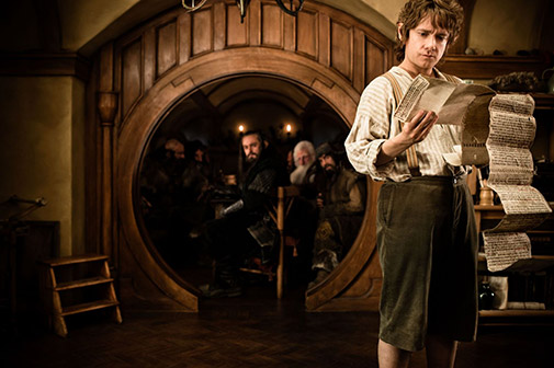 Bilbo looks at some papers while the dwarves look on from behind