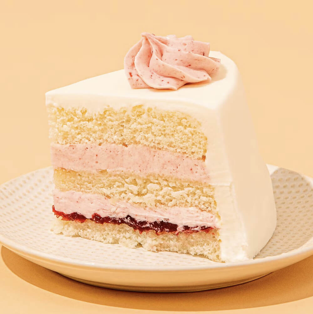 slice of cake with white and pink frosting and layers of white cake, pink frosting, and rapsberry jam