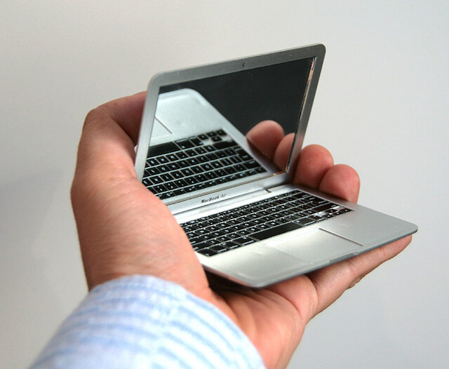 a hand holding a tiny macbook that’s a compact mirror