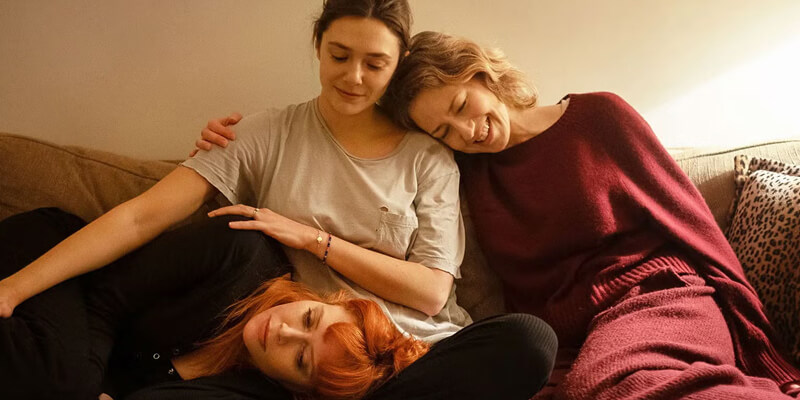 three women on the couch: Carrie Coon leans on Elizabeth Olsen’s shoulder who has Natasha Lyonne’s head in her lap