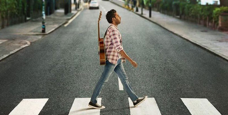a man with a guitar crosses the famous Abbey Road crosswalk