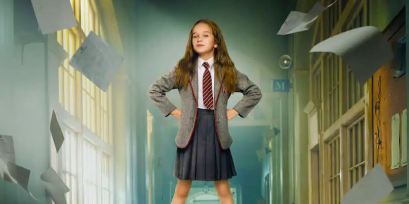 Matilda stands triumphantly in a hallway with her hands on her hips