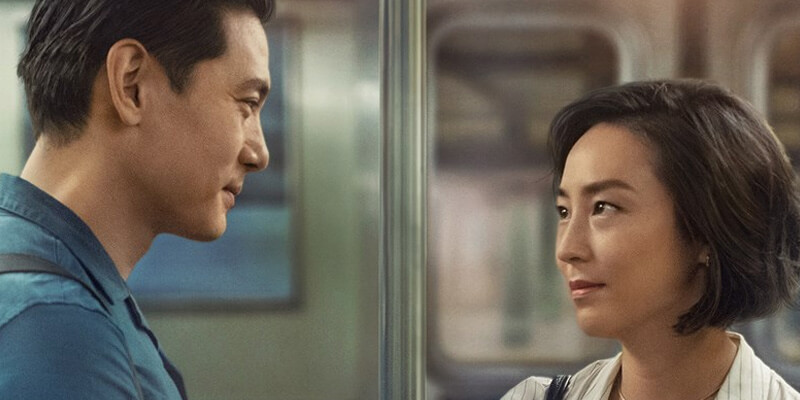 Greta Lee and Teo Yoo look at each other on a train