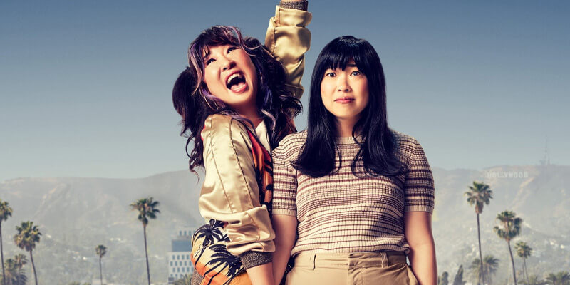 a basically dressed Awkwafina looks concerned next to a pigtailed Sandra Oh who is excitedly raising her arm in the air