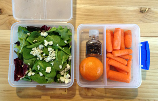 open bento box cube with salad in one compartment, carrots, and an orange