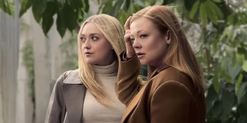 Dakota Fanning and Sarah Snook, each in neutral jackets, against greenery of an upscale backyard