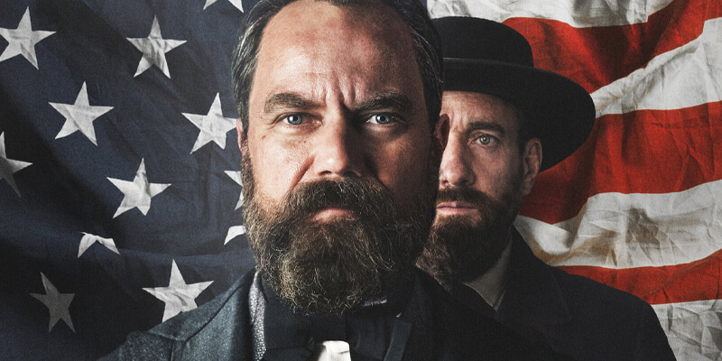 Michael Shannon as Andrew Garfield in front of Matthew Macfadyen as Charles J. Guiteau, both in front of the American flag