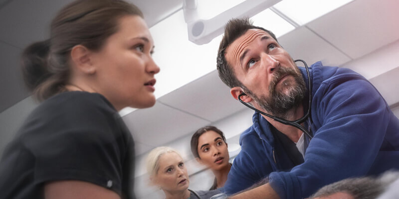 action shot of Noah Wyle and Isa Briones as doctors leaning over a patient, Katherine LaNasa and Supriya Ganesh behind them
