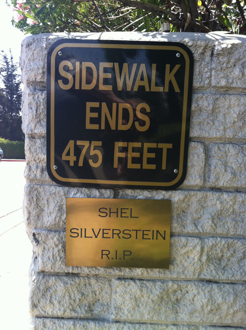 two signs on a brick wall, the first says “Sidewalk ends 475 feet” and the second says “Shel Silverstein R.I.P.”