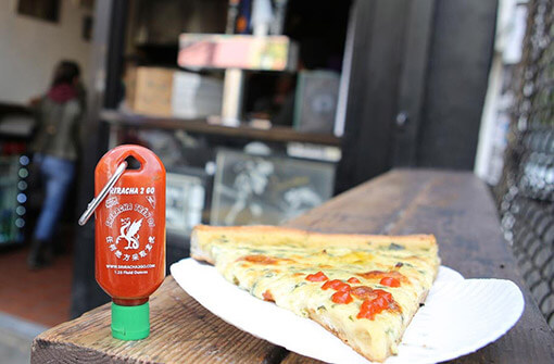 a piece of pizza and a small bottle of sriracha on a keychain